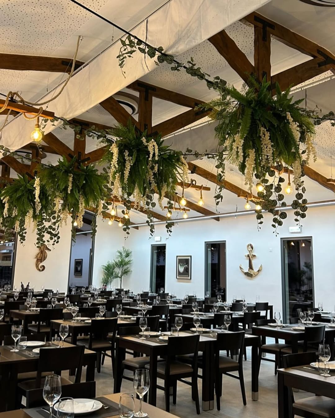 Sala com mesas pretas, vigas de madeira e plantas penduradas