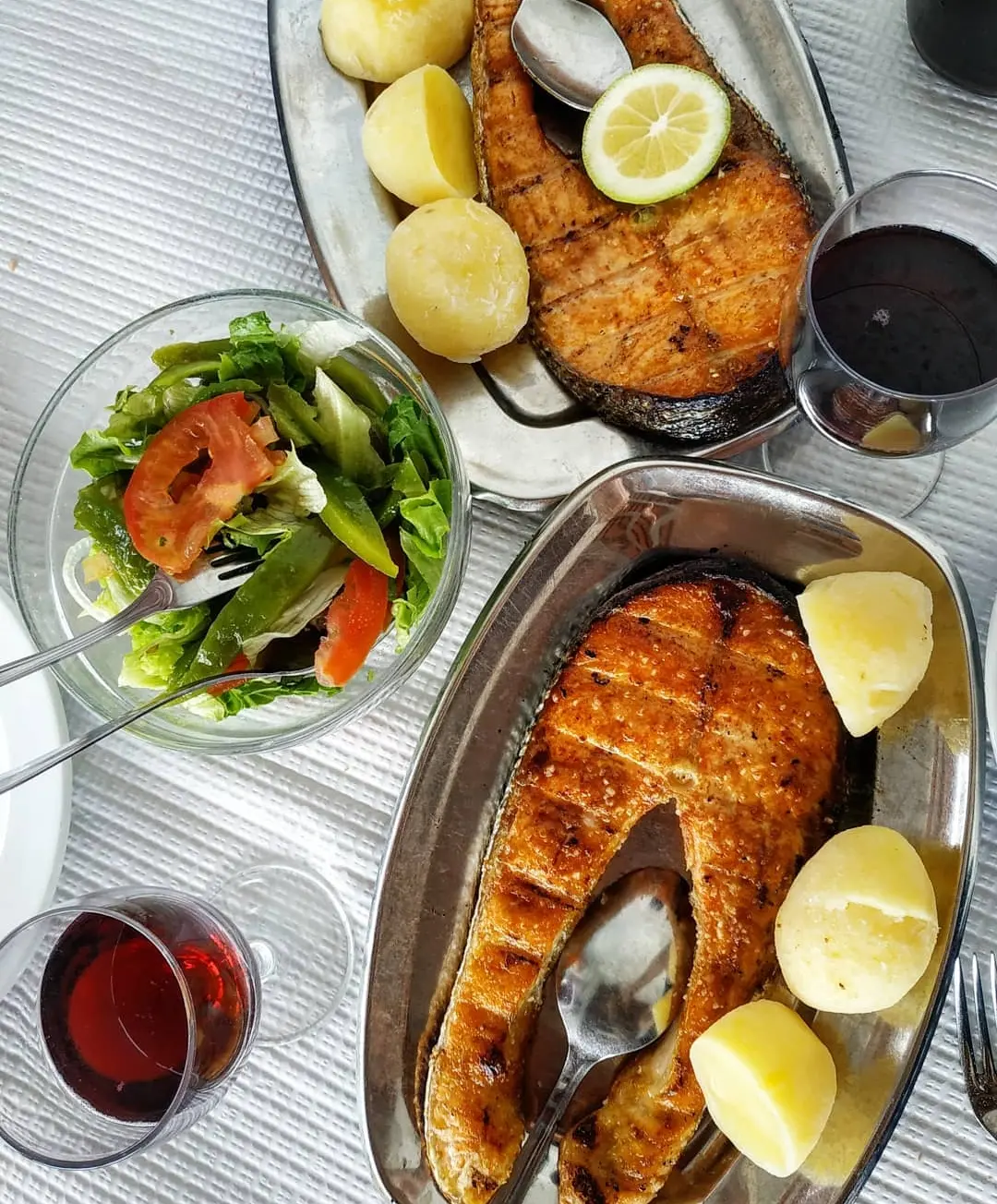 Peixe assado com limão e batata cozida, com salada e vinho tinto à mesa